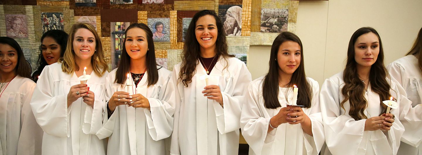 Five students in grad gowns hold candles at Baccalaureate Mass on May 24, 2018.